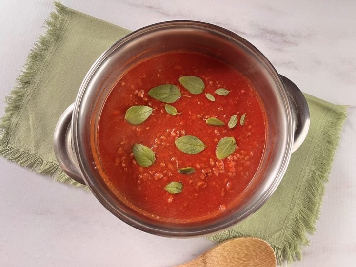 Molho vermelho com carne moída finalizado com folhas frescas de manjericão por cima.