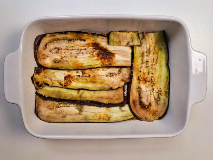 Camada de carne moída e camada de berinjela em uma travessa.