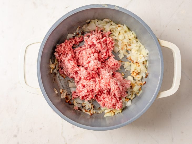 Uma panela com a carne moída, o alho, a cebola e temperos.