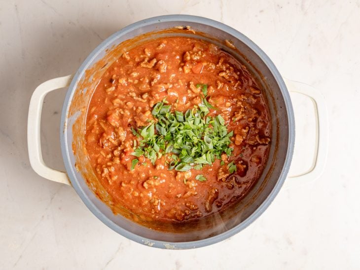 Uma panela com molho de carne moída finalizado com cheiro-verde.