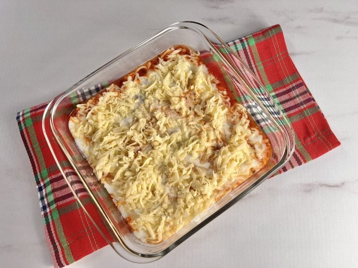 Um refratário forrado com molho de calabresa e coberto com massa de lasanha, molho branco e queijo.