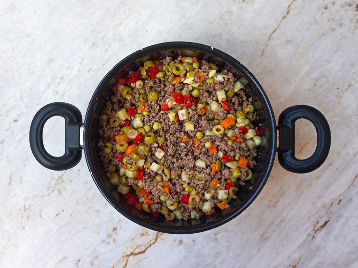 Seleta de legumes, azeitonas e pimentão adicionados a panela.