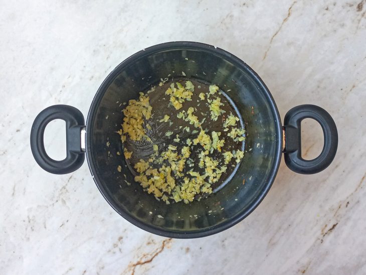 Alho e cebola refogando em uma panela com óleo.