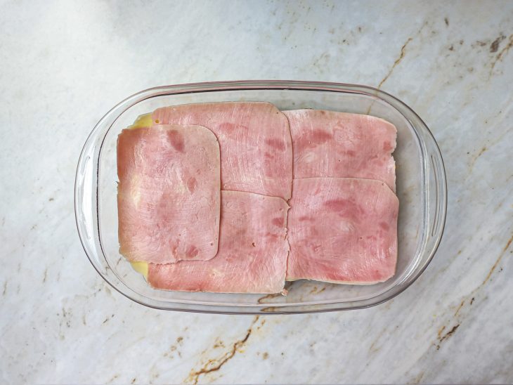 Camadas de queijo mussarela e presunto adicionados a travessa.