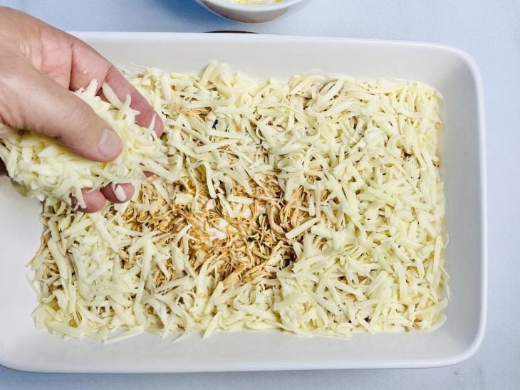 Refratário com camadas de molho branco, massa de lasanha, frango desfiado e queijo.