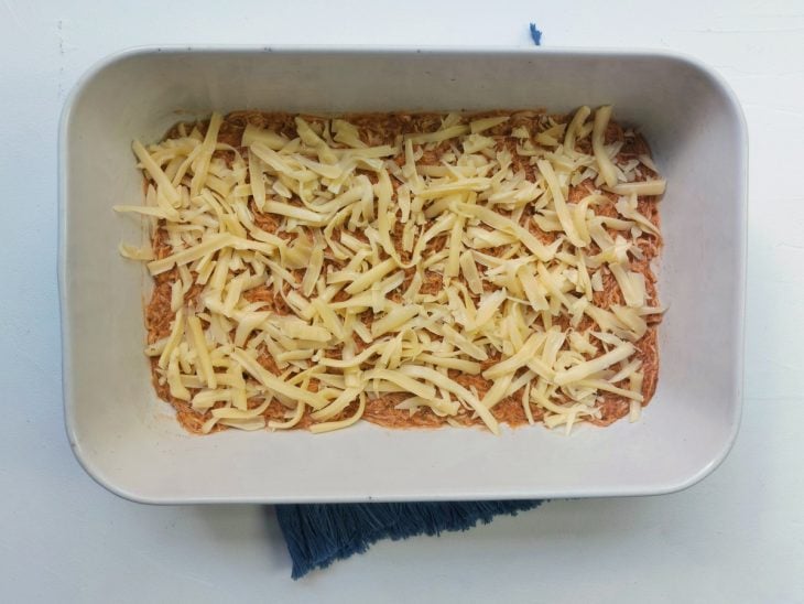 Um refratário com uma camada de molho e uma de queijo fatiado por cima.