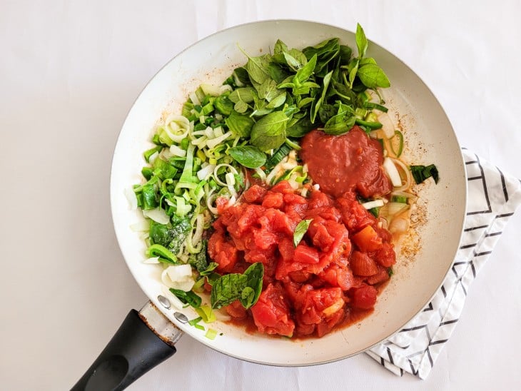 Uma frigideira contendo alho-poró, pimentão verde picados, extrato de tomate, tomate e manjericão.