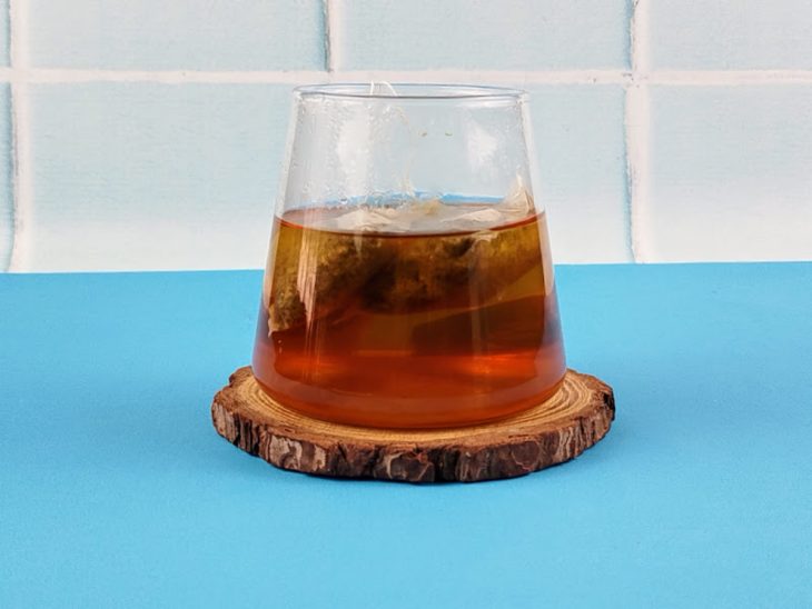 Sachê de chá infusionando em um copo de vidro com água.
