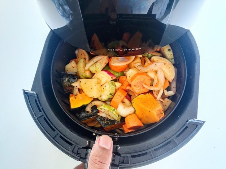 Uma airfryer contendo legumes picados sendo assados.