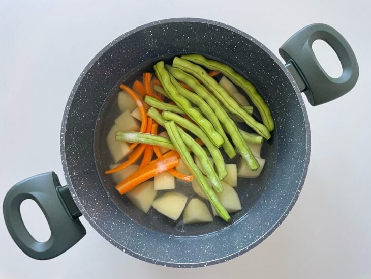 Batatas, cenoura e vagens sendo colocadas em panela com água e sal.