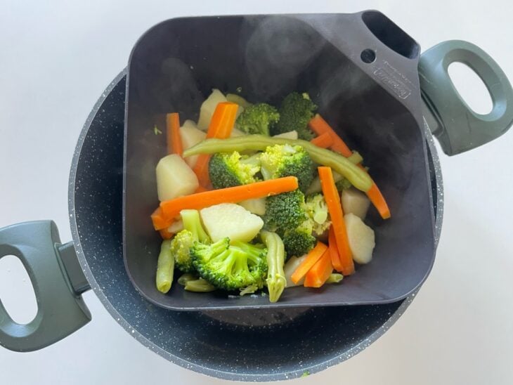 Legumes cozidos sendo escorridos e resfriados rapidamente em água fria.