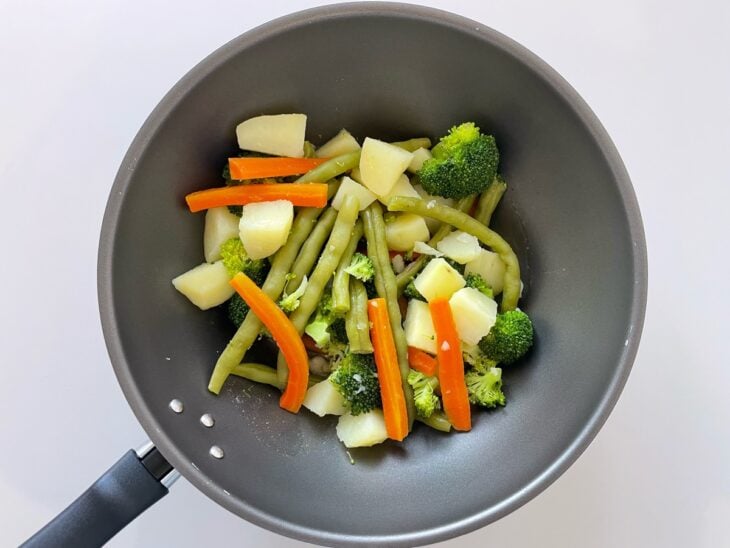 Legumes cozidos sendo adicionados à frigideira e envolvidos na manteiga aromatizada.