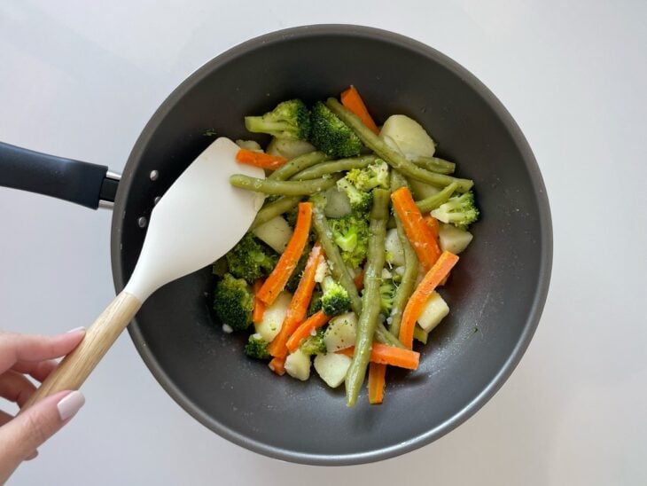 Legumes sendo salteados e temperados com sal e pimenta-do-reino.
