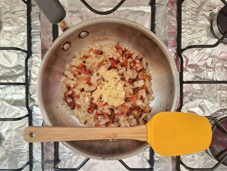 Uma panela com banha, bacon, alho e cebola a dourar.