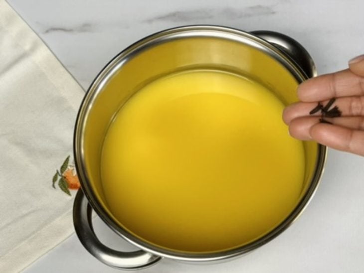 Uma panela com o suco de laranja coado, açúcar e cravos-da-índia.