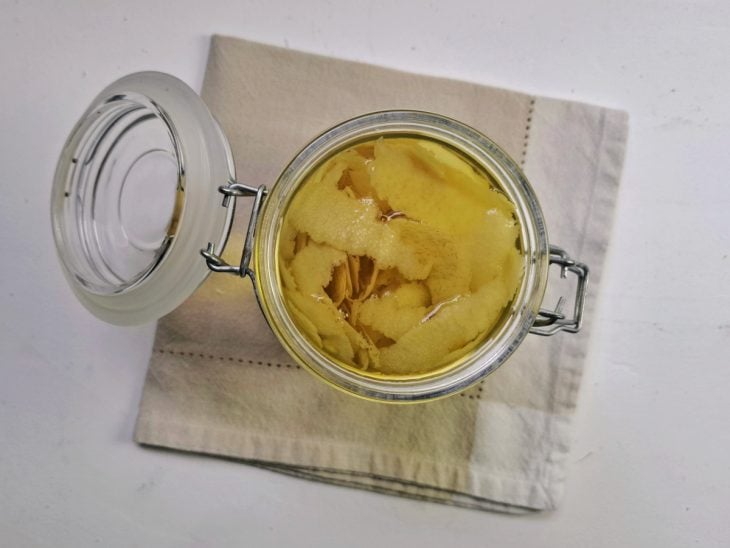 Pote hermético com cascas de limão e calda adicionada.