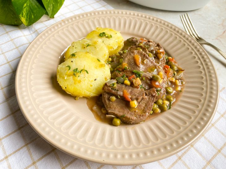 Língua com molho servida com batata em um prato individual.
