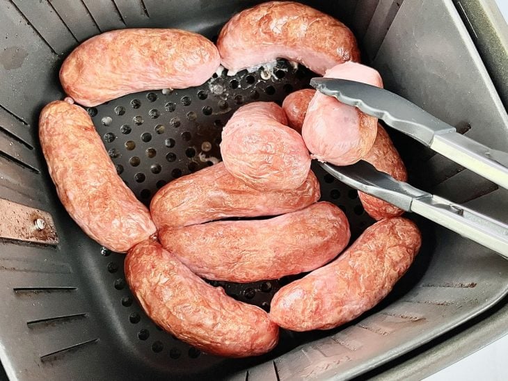 Gomos de linguiça virados com auxílio de um pegador.