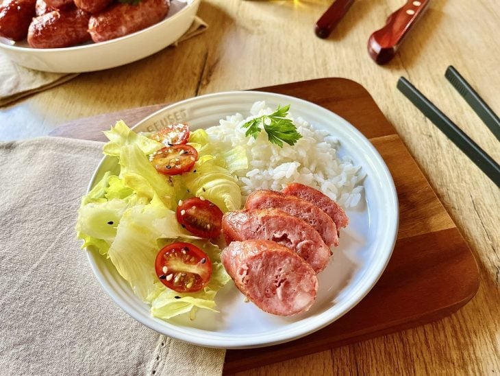 Linguiça preparada na Air Fryer servida com arroz e salada em um prato redondo branco.