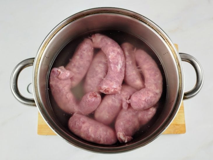 Gomos de linguiça submersas em água dentro de uma panela.