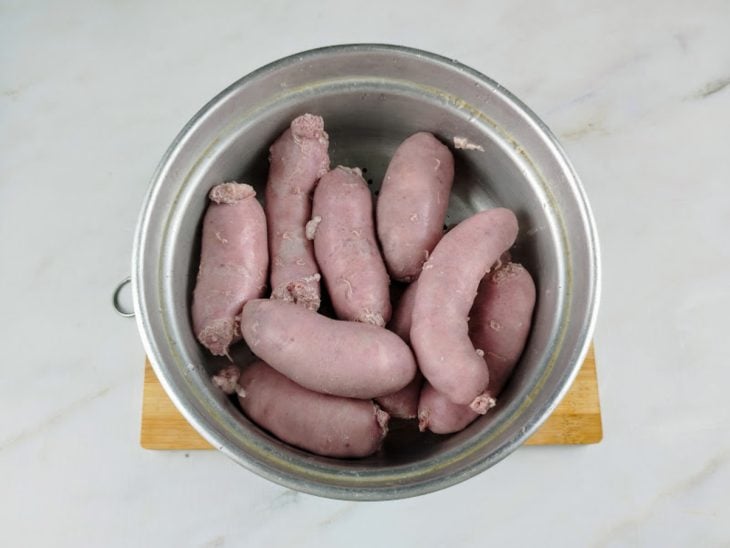 Gomos de linguiça cozidas em um recipiente de alumínio.