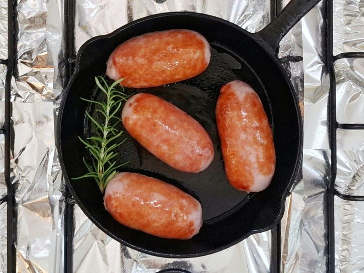 Gomos de linguiça dourados na frigideira com uma erva na frigideira.