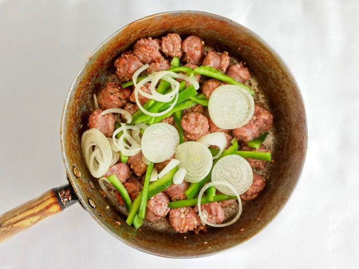 Pimentão e cebola adicionados na frigideira com linguiça toscana.