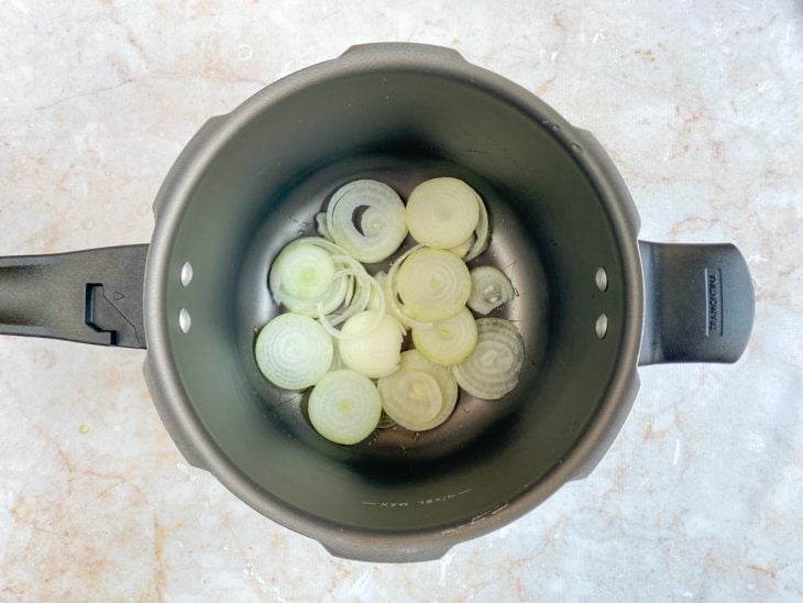 Cebolas acomodadas ao fundo da panela de pressão.