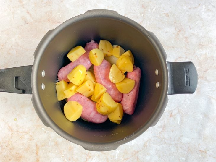 Gomos de linguiça e batatas temperadas acomodadas na panela de pressão.