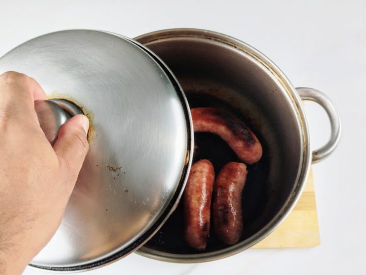 Panela com linguiças a ser tampada.