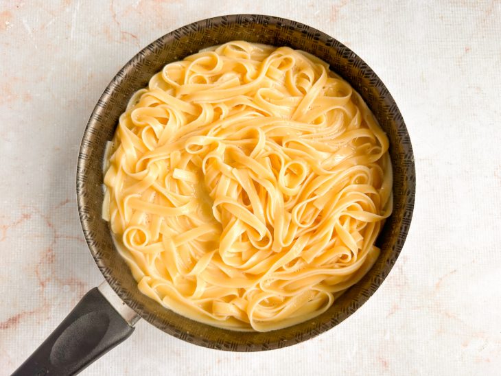 Molho cremoso envolvendo o linguine dentro da panela.