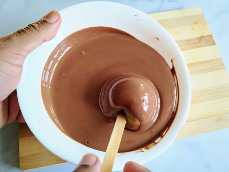 Uma maçã recebendo a cobertura de chocolate.