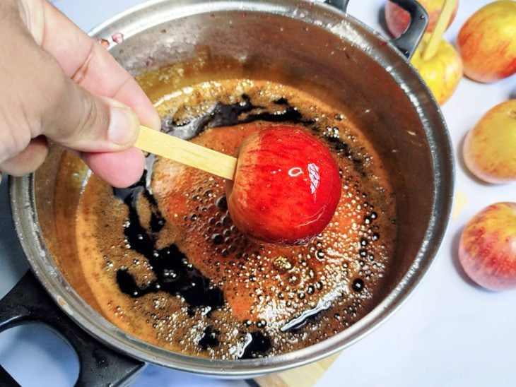 Uma maçã sendo inserida em uma panela com calda.
