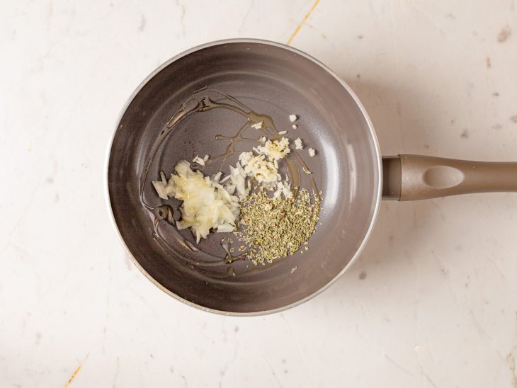 Alho, cebola e orégano dourados em uma panela.