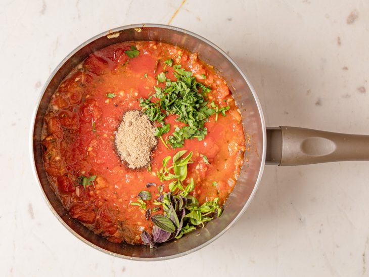 Passata de tomate, sal, salsinha, manjericão e açúcar mascavo em uma panela.
