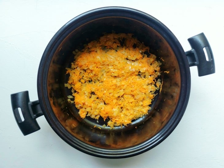Uma panela contendo azeite, cebola, alho e cenoura ralada.