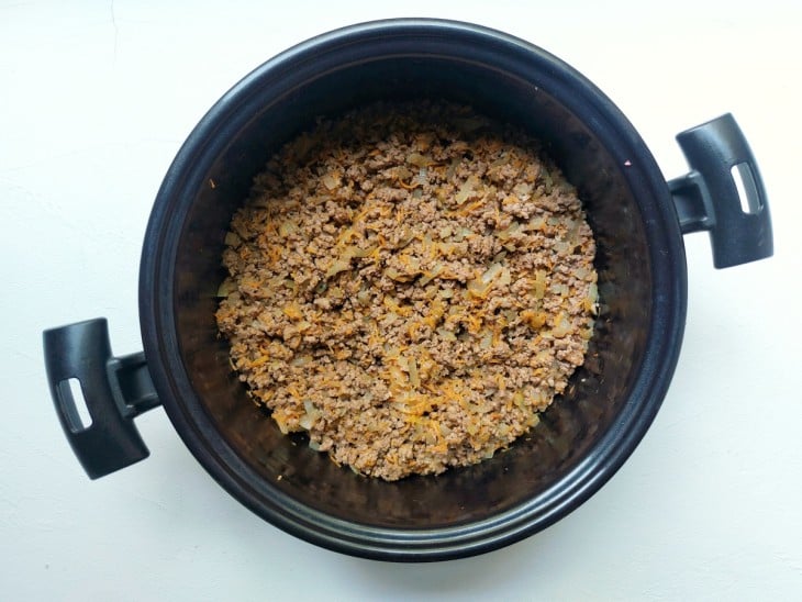 Uma panela contendo azeite, cebola, alho, cenoura ralada e carne moída.