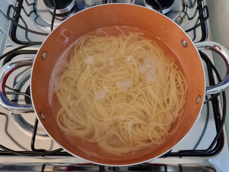 Macarrão cozinhando na água em uma panela de fundo laranja.