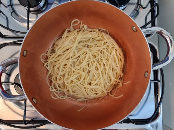 Macarrão cozido adicionado na panela de fundo laranja com o alho e óleo fritinhos.