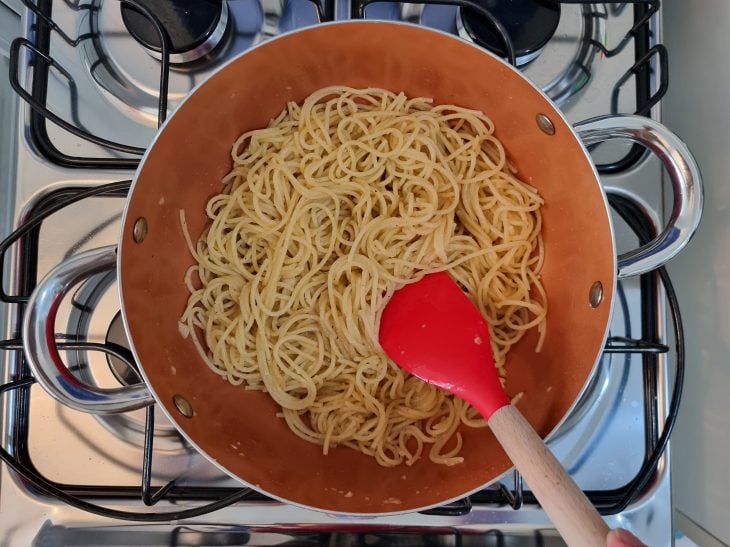 Macarrão alho e óleo sendo mexido com uma espátula.