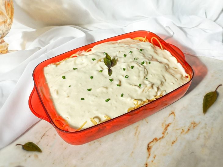 Macarrão ao molho branco simples pronto para consumo servido em um recipiente retangular vermelho.