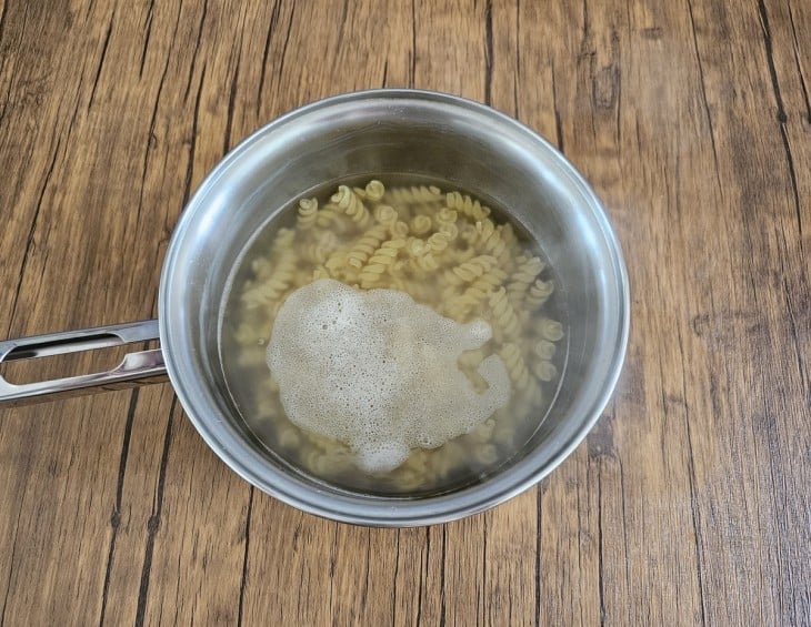 Uma panela de ferro com água fervente e o macarrão dentro.