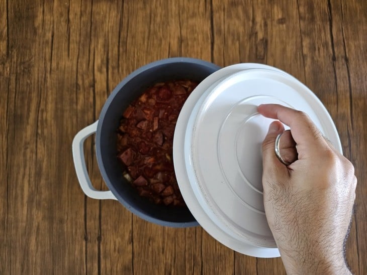 Colocando a tampa de cor branca na panela de cor cinza, deixando entreaberta, enquanto os ingredientes cozinham.