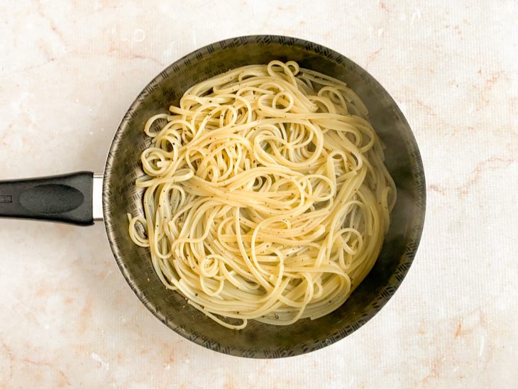 Macarrão cozido e uma concha de água adicionados a frigideira com pimenta.