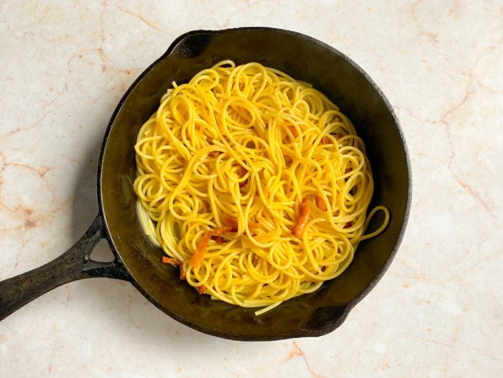 Frigideira com macarrão, bacon e um pouco da água do cozimento do macarrão.