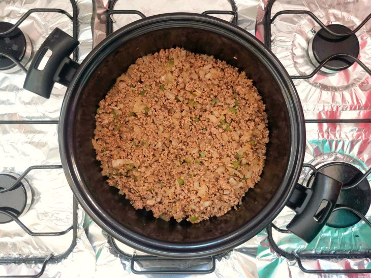 Uma panela refogando cebola, alho, carne moída e temperos.