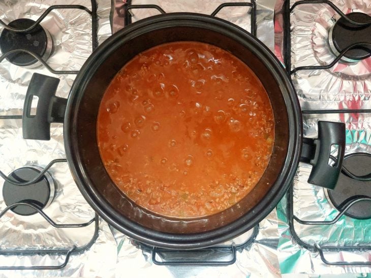 Uma panela refogando cebola, alho, carne moída, tomate, molho de tomate e temperos.