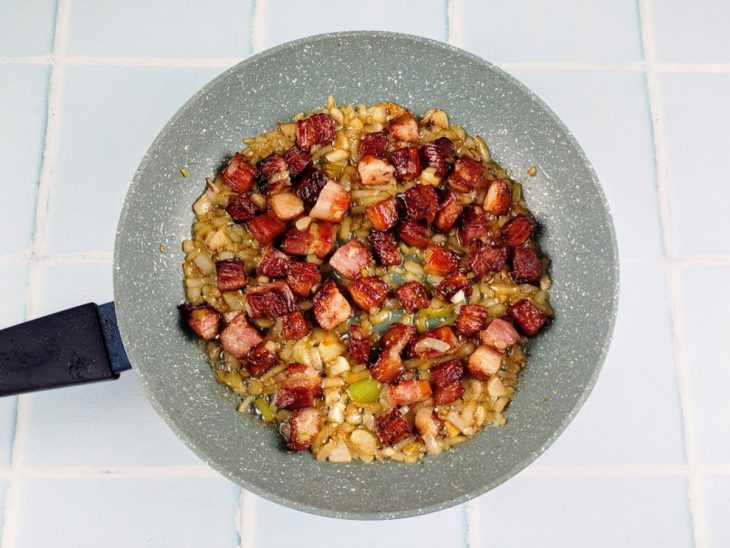 Bacon, alho e cebola refogados em uma frigideira.