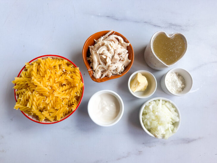 Ingredientes organizados na bancada com macarrão, frango desfiado e cebola picada separados.