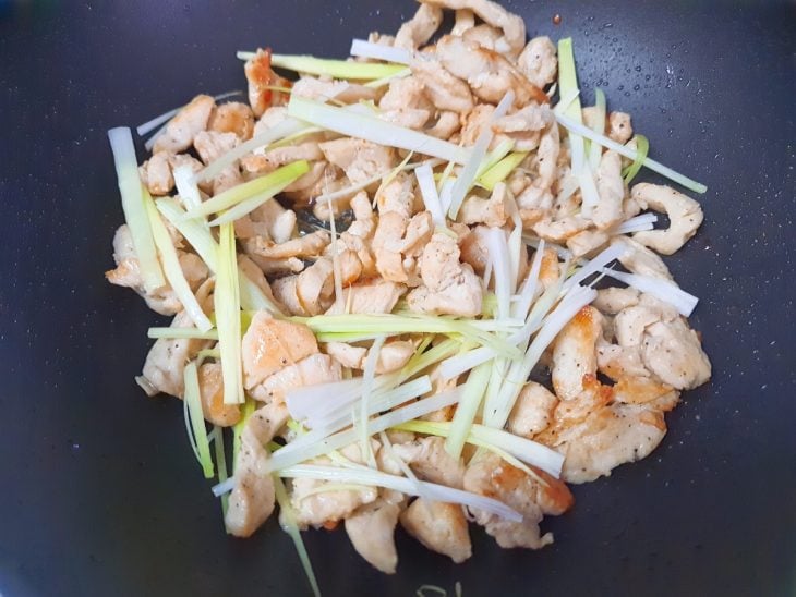 Uma frigideira com o frango e o alho-poró.